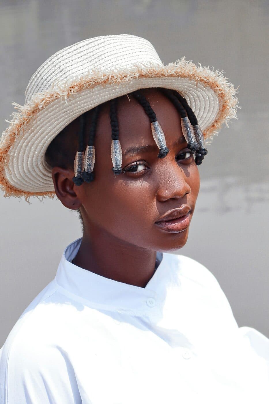 A person wearing a straw boater hat over beaded box braids.